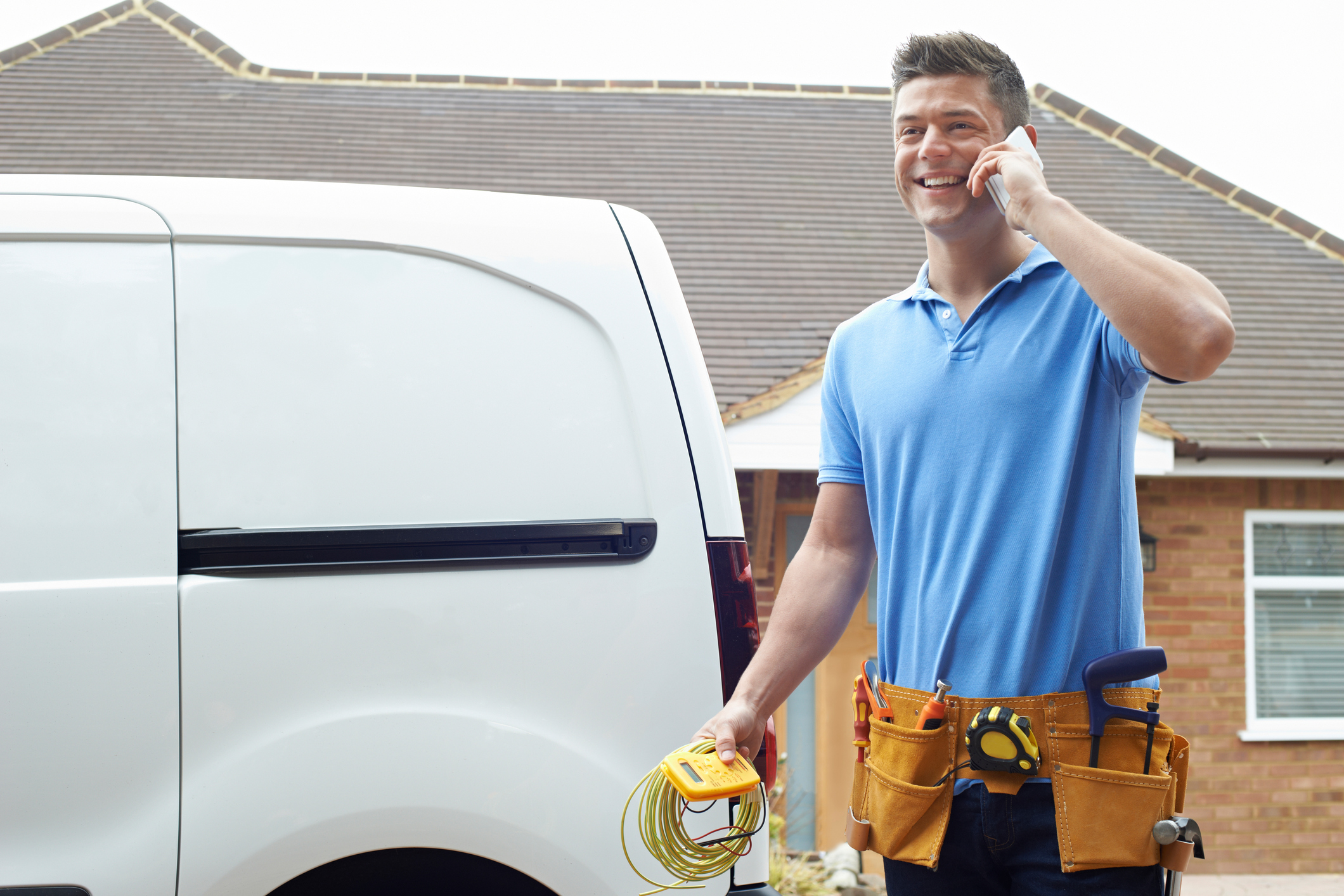 HVAC technician standing in front of work van while talking on the phone